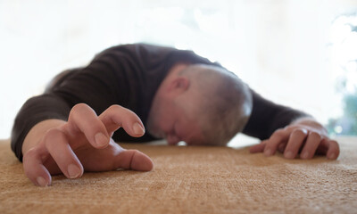 A man lies helpless on the floor, he is sick. The background is light.