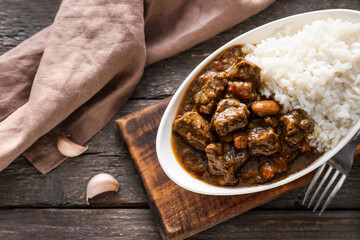 Plate with tasty beef curry and rice on wooden background