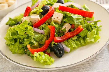 Plate with fresh Greek salad on light wooden background, closeup