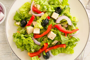 Plate with fresh Greek salad on light wooden background, closeup