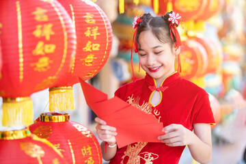 Asian Happy little girl wearing red traditional Chinese cheongsam decoration holding red envelopes in hand and lanterns with the Chinese text Blessings written on it Is a Fortune blessing for Chinese