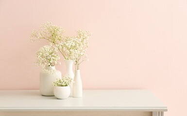 Vases with beautiful gypsophila flowers on table near light wall