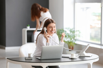 Young woman gossiping while talking by phone in office
