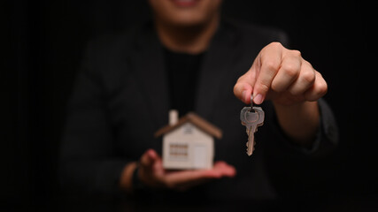 Cropped shot young man holding house key and house model. Insurance or loan real estate concept.