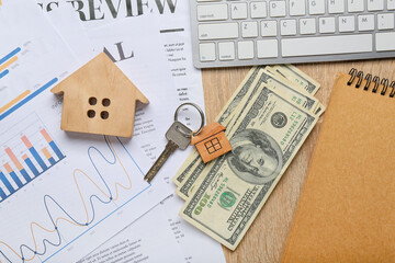 Toy house with key, money, stationery and computer keyboard on wooden background