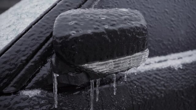 Folded car side mirror, icy close-up. The car is covered with ice after freezing rain in sub-zero temperatures.