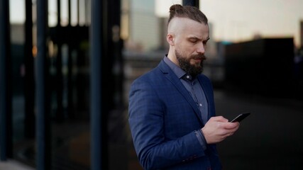 confident and successful businessman is surfing internet by smartphone on street