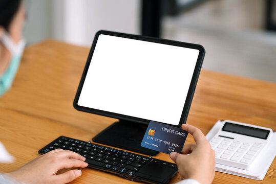 Close up of woman hands holding credit card and using laptop, tablet blank white screen. Online shopping concept. - Powered by Adobe