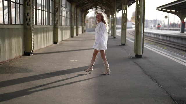 naive and romantic woman is walking in empty old train station, playing with her long hair