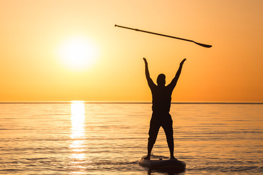 A man in the sea on a SUP board throws an oar into the air. Standup paddleboarding.