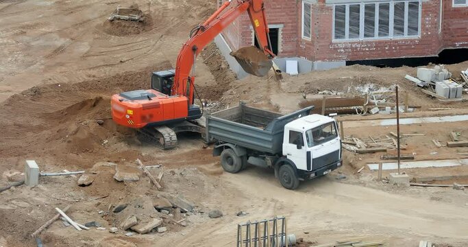 An excavator loads sand into a truck. Construction of a shopping center.