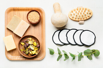 Set of bath supplies with reusable cotton pads and eucalyptus branch on light background