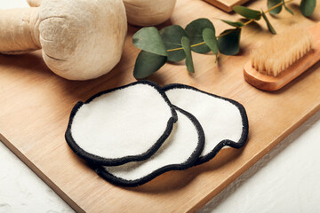 Wooden board with reusable cotton pads and herbal bags on light background, closeup