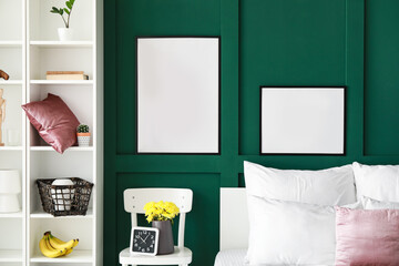 Blank poster frames hanging on green wall in modern bedroom