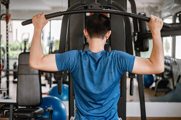 Training gym concept a male teenager using a gym equipment pulling his both muscular arms against...