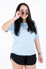 Obraz premium Portrait studio shot of Asian chubby plump healthy long black hair female model in blue casual shirt standing smiling look at camera holding touching take off vintage sunglasses on white background