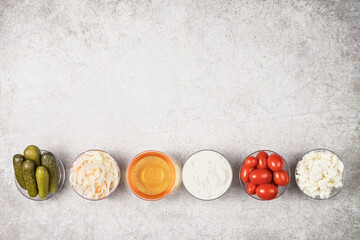 A variety of fermented foods for gut health. Bowls on a gray background. Cucumbers, tomatoes, sauerkraut, yogurt, cottage cheese, apple cider vinegar. Copy space.