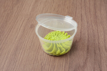 Wasabi sauce in a clear plastic container for delivery. On a wooden surface, close-up