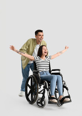 Young woman in wheelchair and her husband on light background