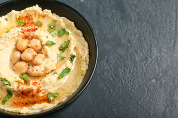 Bowl with delicious hummus on dark background, closeup