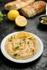 Plate with delicious hummus and lemon on dark background
