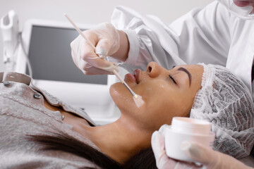 Cosmetology. Cosmetologist applies a cleansing mask on black woman face with a brush. Cosmetic...