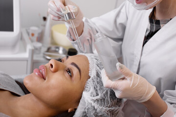 A cosmetologist drips a cosmetic serum on a woman's forehead during the beauty procedure. Close-up portrait of the client. Professional skin care in salon.