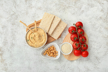 Fototapeta na wymiar Bowl with delicious hummus, crackers and tomatoes on light background