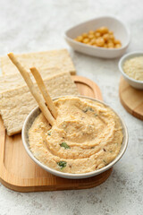 Bowl with delicious hummus and crackers on light background, closeup