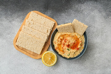 Bowl with delicious hummus, crackers and lemon on grey background