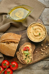 Bowl with delicious hummus, bread, tomatoes and oil on wooden background