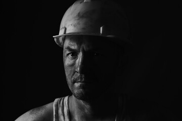 Portrait miner in helmet and undershirt with dirty face.
