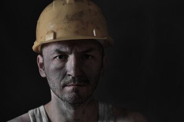 Portrait miner in helmet and undershirt with dirty face.