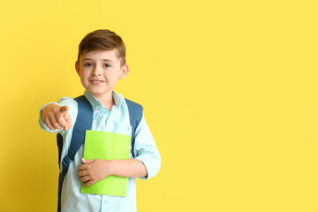 Little school boy pointing at viewer on color background