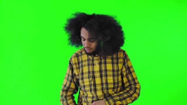 A young man with an African hairstyle on a green background takes out his phone, looks at the message and puts it back in his pocket. Emotions on a colored background
