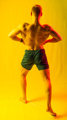 muscular man in blue shorts posing shows, straining his muscles. yellow and red highlights on the...