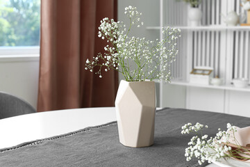 Vase with gypsophila flowers on dining table in room