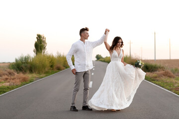 Happy wedding couple dancing on road in countryside