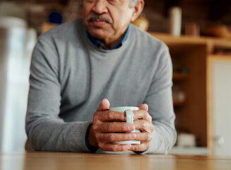 Close up of hands of pensive retired biracial elderly male leaning on modern kitchen counter, holding morning coffee in his hands.