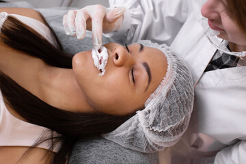 Obraz na płótnie Canvas Applying anesthesia before enlarging lips at beauty salon. Moisturizing the lips during a cosmetic procedure for a young girl. Cosmetology