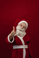 A boy in a Santa Claus costume holds his thumbs up.
