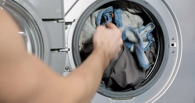 Man puts dirty things in an automatic washing machine. Mens hands load the washing machine with dirty laundry and clothes. Concept of washing at home, everyday life, household chores, homework