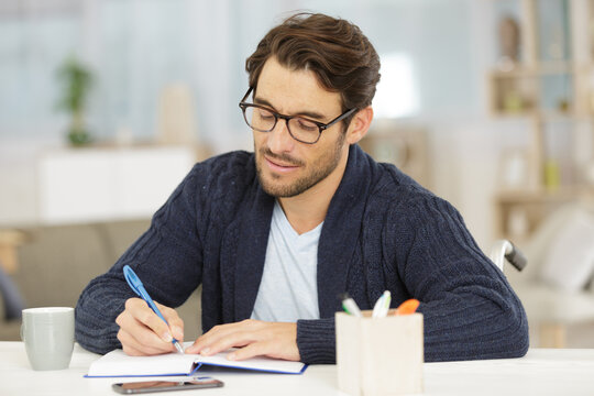 Disabled Man Sat At A Table Writing In A Book