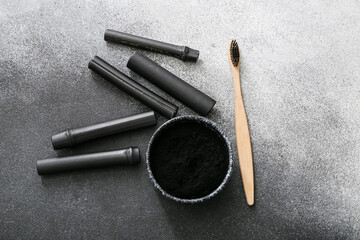 Bowl with activated charcoal tooth powder, bamboo sticks and brush on grunge background