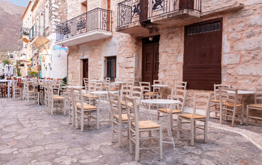 Fototapeta na wymiar Cafe bar open air. Empty seats on cobblestone street, stone wall background, Areopoli, Mani Greece
