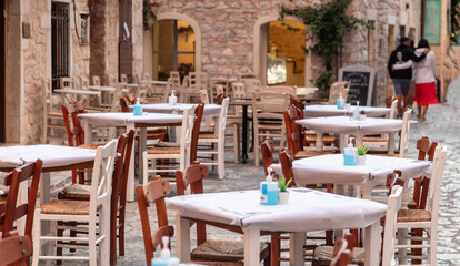 Fototapeta na wymiar Greek tavern outdoor empty seats on cobblestone street, stone wall background, Areopoli, Mani Greece