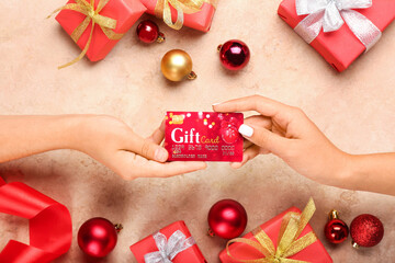 Female hands with gift card and Christmas decor on color background
