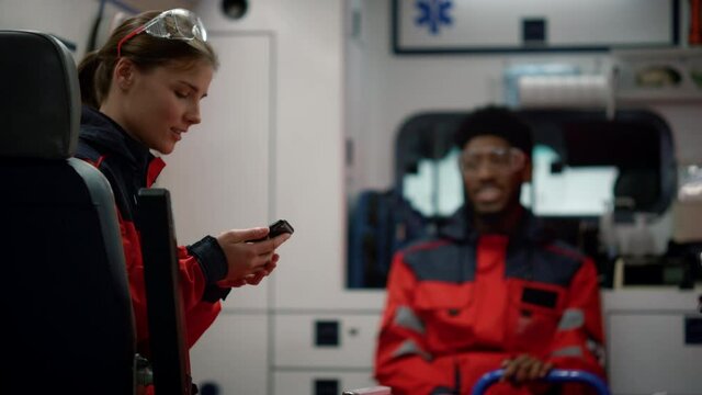 Smiling paramedic doctor talking with afro medical worker in emergency car