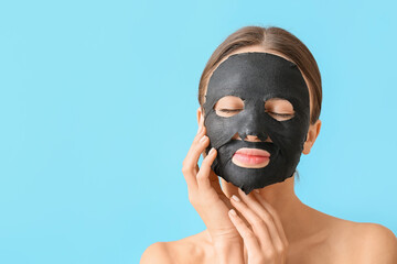 Young woman with activated charcoal mask on her face against color background