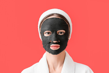Young woman with activated charcoal mask on her face against color background
